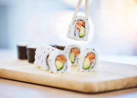 Téléchargez les photos : Sushi, nourriture sur bois avec poisson et manger, saumon et riz avec avocat, sain et luxueux. Cuisine japonaise, restauration avec déjeuner ou dîner, baguettes et fruits de mer, nutrition et gastronomie. - en image libre de droit
