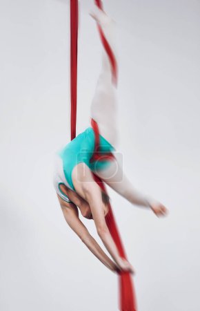 Photo for Sport, acrobat and aerial silk with a woman in air for performance, gymnastics and balance. Young athlete person or gymnast hanging on red fabric and white background with space, art and creativity. - Royalty Free Image