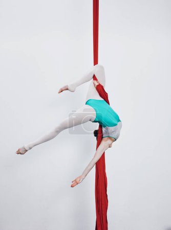 Photo for Aerial silk, acrobat and gymnastics with a woman in air for performance, sports and balance. Young athlete person or gymnast hanging on red fabric and white background with space, art and creativity. - Royalty Free Image