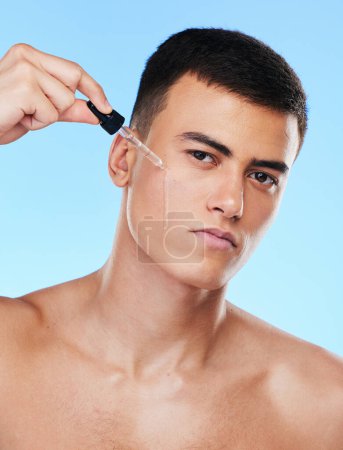 Photo for Man, serum and drop for face in studio with beauty, wellness and facial change by blue background. Young model, oil or hyaluronic acid for glow, shine and cleaning skin with cosmetic transformation. - Royalty Free Image