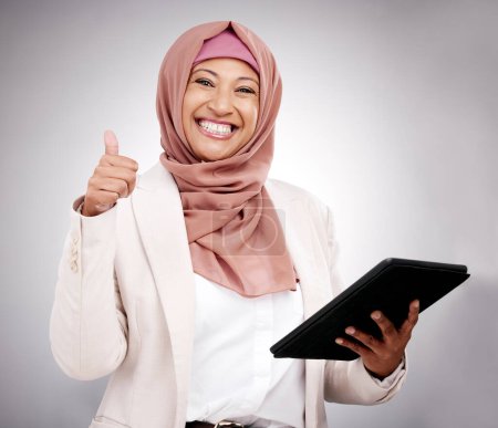 Téléchargez les photos : Pouces levées, tablette et portrait d'une femme musulmane dans un studio faisant des recherches sur Internet. Joyeux, sourire et mature modèle féminin islamique avec la technologie et geste de la main d'accord par fond gris. - en image libre de droit