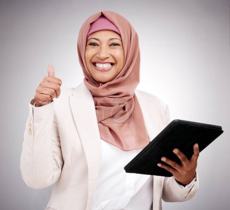 Foto de Pulgares hacia arriba, tableta y retrato de una mujer islámica en el estudio haciendo investigación en Internet. Modelo femenino musulmán feliz, sonriente y maduro con tecnología y gesto de mano de acuerdo por fondo gris - Imagen libre de derechos