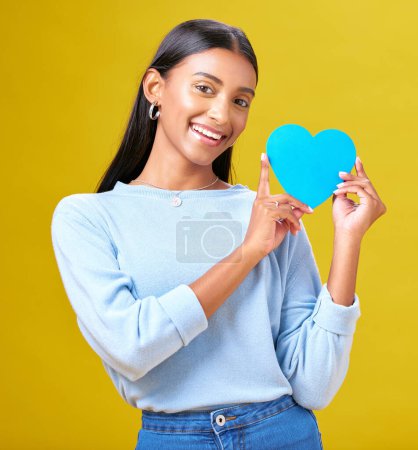 Photo for Portrait, donation and woman with blue heart in studio for help, hope or empathy on yellow background. Face, charity and social media, poster or thank you, support or autism or people with disability. - Royalty Free Image