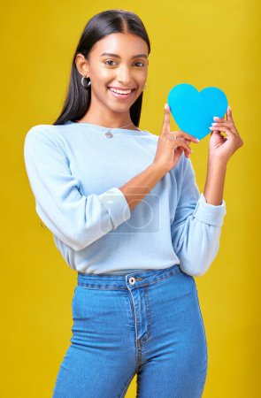 Photo for Portrait, smile and woman with blue heart in studio with help, hope or empathy on yellow background. Face, girl and social media icon for thank you, support and trust or people with loyalty to peace. - Royalty Free Image