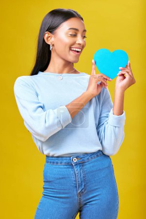 Photo for Donation, smile and woman with blue heart in studio for help, hope or empathy on yellow background. Charity, lady or social media poster for thank you, support for autism or people with a disability. - Royalty Free Image