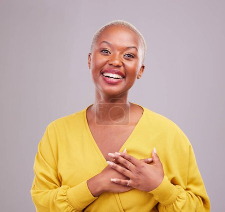 Téléchargez les photos : Reconnaissant, sourire et portrait d'une femme noire dans un studio avec une attitude douce, heureuse et positive. Empathie, gratitude et jeune modèle féminin africain avec geste de remerciement isolé par fond gris. - en image libre de droit