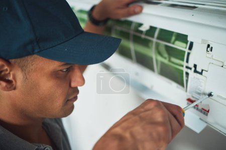 Photo for Face, hand and a man for aircon repair or maintenance in an office for circulation or central heating. Construction, tools or screwdriver with an engineer working on an air conditioning unit closeup. - Royalty Free Image
