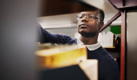 Photo for Knowledge, research and black man in a library search and learning on campus for studying and education in college. Smart, clever and young person in an academy with books on a shelf for an exam. - Royalty Free Image