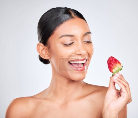 Photo for Wellness, happy and woman with a strawberry in studio for healthy diet snack for nutrition. Health, beauty and young Indian female model with fruit for natural skin detox routine by white background - Royalty Free Image
