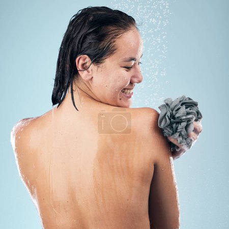 Photo for Happy woman, shower and back in water drops with loofah in hygiene, grooming or washing against a blue studio background. Rear view of female person in body wash, cleaning or wet skincare in bathroom. - Royalty Free Image