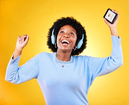 Foto de Mujer negra feliz, teléfono y auriculares para escuchar música sobre un fondo de estudio amarillo. Mujer africana sonrisa, afro o móvil aplicación de teléfono inteligente bailando a pista de audio, sonido o podcast. - Imagen libre de derechos