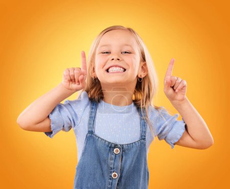 Photo for Child, happy portrait and pointing up in studio for advertising, announcement or promotion. Excited young girl kid on a orange background for hand gesture, sale or sign for attention or marketing. - Royalty Free Image