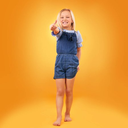 Photo for Happy, portrait of child and thumbs up in studio for support, like emoji or yes approval. Excited girl kid on orange background or space for hand gesture, barefoot or sign for agreement or thank you. - Royalty Free Image