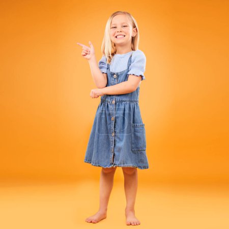 Photo for Pointing, happy portrait and child in studio for advertising, announcement or promotion. Excited barefoot girl kid on a orange background for hand gesture, sale or sign for mockup space or fashion. - Royalty Free Image