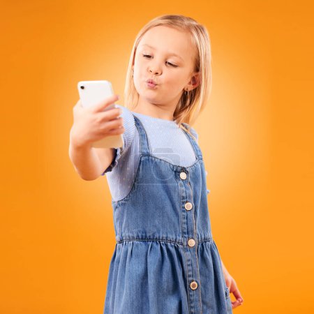 Photo for Kiss, selfie or child in studio with confidence or mockup space for photograph memory on web. Fashion, orange background or young girl taking pictures online on a social media app to post on internet. - Royalty Free Image