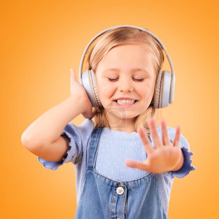 Photo for Headphones, dancing or child streaming music to relax with freedom in studio on orange background. Smile, excited and happy girl listening to a radio song, sound or audio on an online subscription. - Royalty Free Image