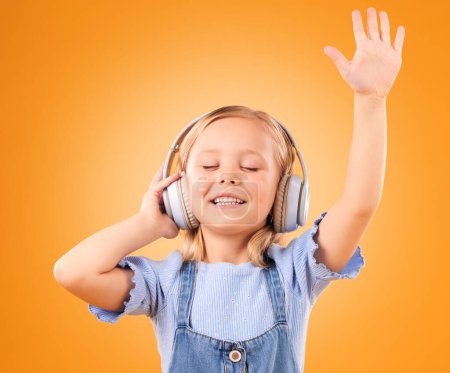 Photo for Headphones, happy or child streaming music to relax with freedom in studio on orange background. Hand up, singing or girl singer listening to a radio song, sound or gospel on an online subscription. - Royalty Free Image