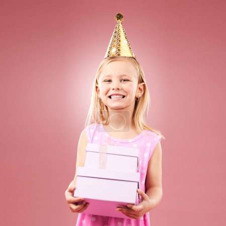 Téléchargez les photos : Cadeau, fête d'anniversaire et portrait d'enfant avec un chapeau pour les vacances ou une célébration heureuse. Fille excitée sur un fond rose pour la surprise, cadeau prix ou célébrer gagner à l'événement avec un cadeau et la joie. - en image libre de droit