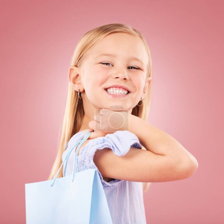 Photo for Portrait, girl kid with shopping bag or gift, customer and purchase with fashion or birthday party on pink background. Retail, smile and child with present, luxury and event with happiness in studio. - Royalty Free Image