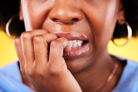 Closeup, woman and biting hands in anxiety, nervous or mental health disorder against a yellow background. Mouth of anxious female person in stress, breakdown or issues and problems in bad habit.