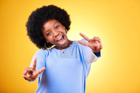 Photo for Peace, hand sign and portrait of a woman in studio with fun emoji, excited face and v symbol. Happy african person on yellow background for positive mood, motivation and review with gesture or vote. - Royalty Free Image