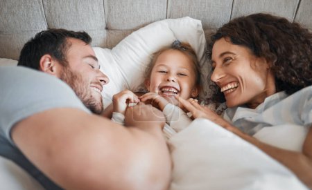 Photo for Family, bedroom and parents laughing with their daughter in the morning to relax after waking up together. Kids, love or smile with a man, woman and cute child having fun in the bed from above. - Royalty Free Image