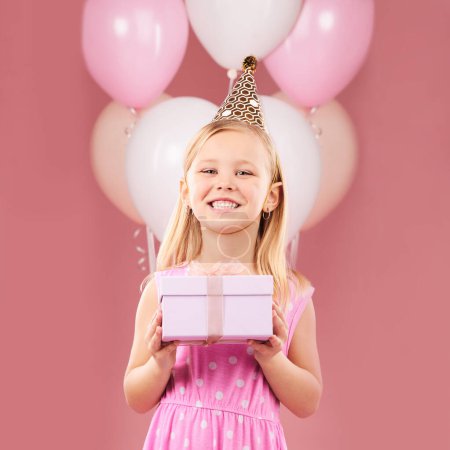 Foto de Presente, cumpleaños y retrato de un niño con globos en estudio para fiesta, fiesta o feliz celebración. Chica emocionada sobre un fondo rosa con caja de regalo, sombrero y paquete sorpresa con una sonrisa. - Imagen libre de derechos