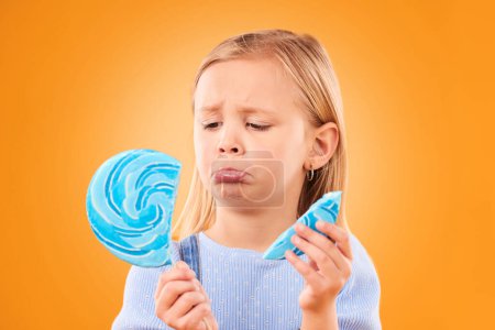 Photo for Children, candy and a sad girl with a broken lollipop on an orange background in studio looking upset. Kids, sweets and unhappy with a female child holding a cracked piece of a sugar snack in regret. - Royalty Free Image