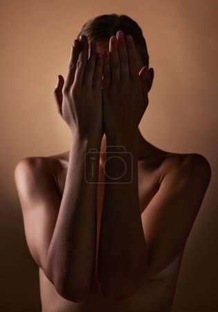 Photo for Woman, body and hands covering face on dark brown background in studio for creative aesthetic, art deco and skin texture. Shy person, model and hide in shadow for nude beauty, wellness and sensuality. - Royalty Free Image