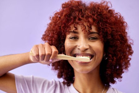 Foto de Rostro, sonrisa y mujer cepillándose los dientes con madera en estudio aislado sobre fondo púrpura. Retrato, cepillo de dientes de bambú y limpieza de personas felices para una higiene ecológica, salud dental o sostenibilidad. - Imagen libre de derechos