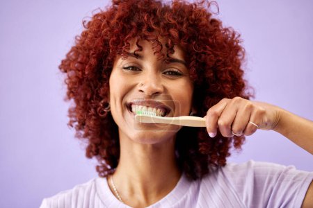 Foto de Rostro, sonrisa y mujer cepillándose los dientes con bambú en estudio aislado sobre fondo púrpura. Limpieza de retratos, cepillos de dientes de madera y personas felices para una higiene ecológica, salud dental o sostenibilidad. - Imagen libre de derechos