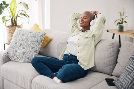 Téléchargez les photos : Femme noire, méditation et écoute de podcast pour se détendre avec des écouteurs dans la maison, salon ou la paix sur le canapé. Musique, technologie ou bonheur sur le visage de la personne avec calme, état d'esprit ou bien-être dans l'appartement. - en image libre de droit