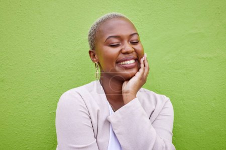 Foto de Mujer negra feliz, tranquila y joven junto a una pared verde con joyas y atuendos de moda, con clase y elegantes. Moda, sonrisa y pacífico modelo femenino africano con felicidad, actitud positiva y segura - Imagen libre de derechos