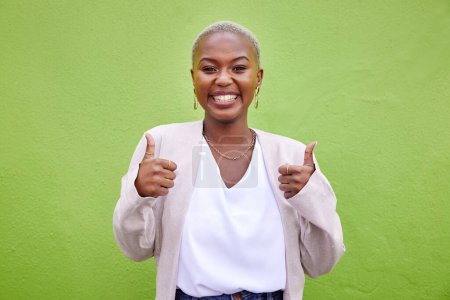Photo for Happy, thumbs up and portrait of black woman by a green wall with classy and elegant jewelry and outfit. Happiness, excited and African female model with positive and confident attitude with fashion - Royalty Free Image