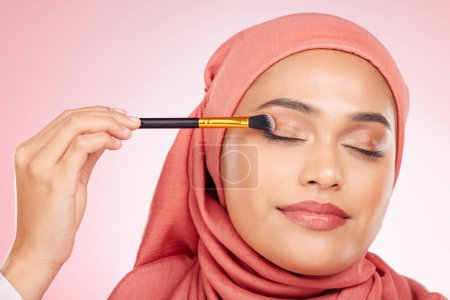Photo for Beauty, makeup and muslim woman in studio with a brush for eyeshadow, glamour or face routine. Cosmetics, self care and young islamic female model with cosmetology product isolated by pink background. - Royalty Free Image