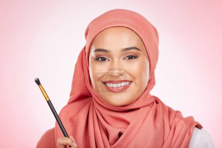 Téléchargez les photos : Beauté, portrait et femme musulmane avec pinceau de maquillage en studio pour le bien-être et les cosmétiques sur fond rose. Soins de la peau halal, visage et femme avec hijab pour des produits de luxe, glamour ou sans danger islamique. - en image libre de droit