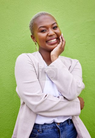 Foto de Feliz, sonrisa y retrato de mujer negra por una pared verde con joyería elegante y elegante y atuendo. Felicidad, modelo femenino emocionado y africano con actitud positiva y segura con la moda - Imagen libre de derechos