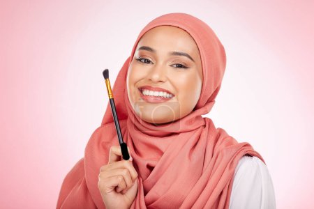 Téléchargez les photos : Portrait, beauté et femme musulmane avec pinceau de maquillage en studio pour le bien-être et les cosmétiques sur fond rose. Soins de la peau halal, visage et femme avec hijab pour des produits de luxe, glamour ou sans danger islamique. - en image libre de droit