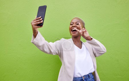 Photo for Woman, selfie and peace or hand sign by a wall or green background with social media. Excited african person with a profile picture, memory and influencer post or vlog with happy emoji outdoor. - Royalty Free Image