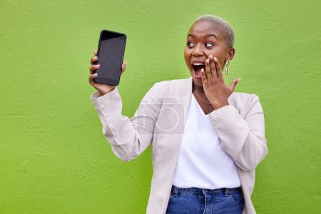 Foto de Mujer, sorpresa y pantalla del teléfono con maqueta por una pared o fondo verde con publicidad wow. Persona africana conmocionada o ganadora con un teléfono inteligente para redes sociales, chat de aplicaciones móviles o espacio en el sitio web. - Imagen libre de derechos