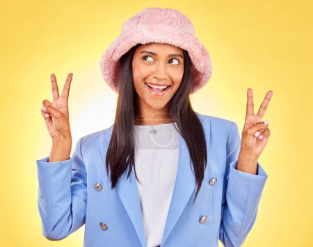 Foto de Moda, signo de paz y cara de mujer india sobre fondo amarillo con sonrisa, actitud positiva y feliz. Emoji, relax y persona en estudio con gesto de mano en accesorios de moda, estilo y sombrero. - Imagen libre de derechos