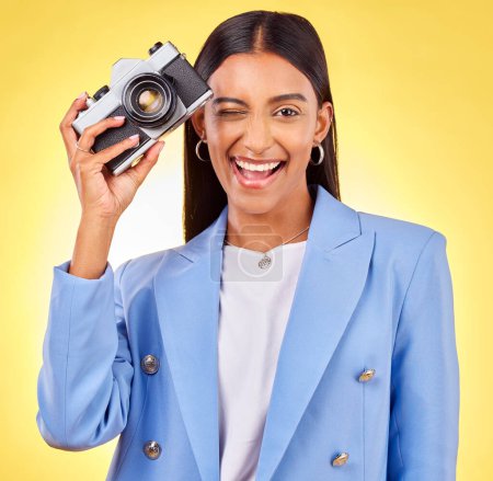 Photo for Camera, photography and woman portrait with a smile and wink for picture in studio. Happy, female person and yellow background with creative, memory and funny emoji face with photographer skill. - Royalty Free Image
