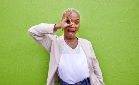 Téléchargez les photos : Parfait, surprise et portrait de femme noire sur un mur vert pour la mode, la revue ou la recherche. Joyeux, ok et une fille africaine ou une personne avec un geste sur un oeil pour wow, cercle ou à la mode sur une toile de fond. - en image libre de droit