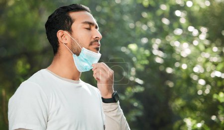 Photo for Relief, breathing and a man with a face mask in nature for fitness, running or exercise. Calm, mockup space and an Asian runner or athlete with covid and breathe after running in a park for cardio. - Royalty Free Image