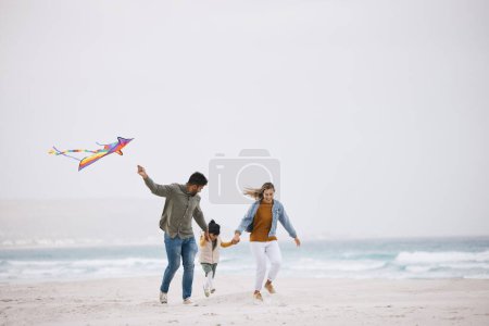Photo for Family, running and flying a kite at beach outdoor with fun energy, happiness and love in nature. Man and woman playing with a girl kid on holiday, freedom adventure or vacation at sea with banner. - Royalty Free Image