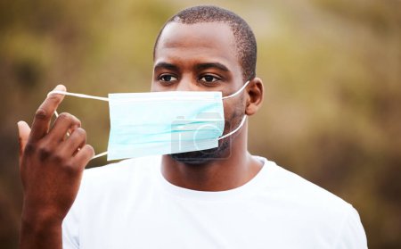 Photo for Corona, outdoor and black man remove mask, regulations and pandemic policy with breathing, health and decrease infection rates. African person, nature and guy take off face cover, safety and freedom. - Royalty Free Image