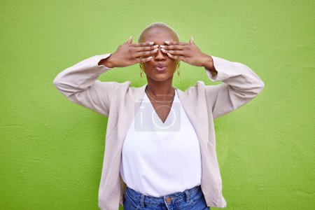 Photo for Cover eyes, playful and a black woman on a green background for comedy, happiness or fun. Pouting, hide or an African girl or model with a shy expression, surprise or funny on a wall in the city. - Royalty Free Image