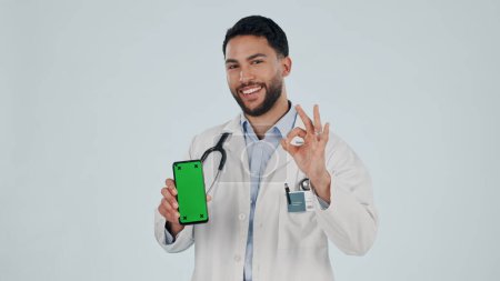 Photo for Doctor, phone green screen and yes hand, success or healthcare support, excellence or ok emoji in studio. Face of medical man for mobile telehealth or services, tracking marker and white background. - Royalty Free Image