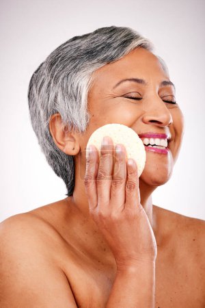 Photo for Face, mature happy woman and beauty sponge for anti aging wellness, morning self care and remove studio makeup. Bathroom grooming pad, eyes closed and relax person with clean skin on white background. - Royalty Free Image