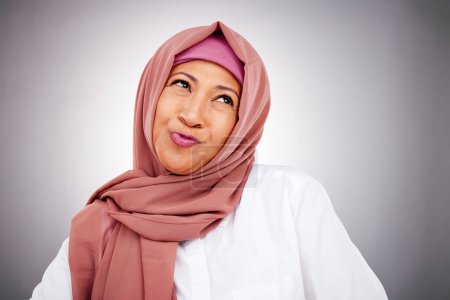 Téléchargez les photos : Mode, sourire et femme musulmane pensant en studio isolé sur un fond gris. Modèle féminin islamique heureux dans le maquillage, les cosmétiques et confiant dans les vêtements à la mode, le hijab traditionnel et l'écharpe élégante. - en image libre de droit